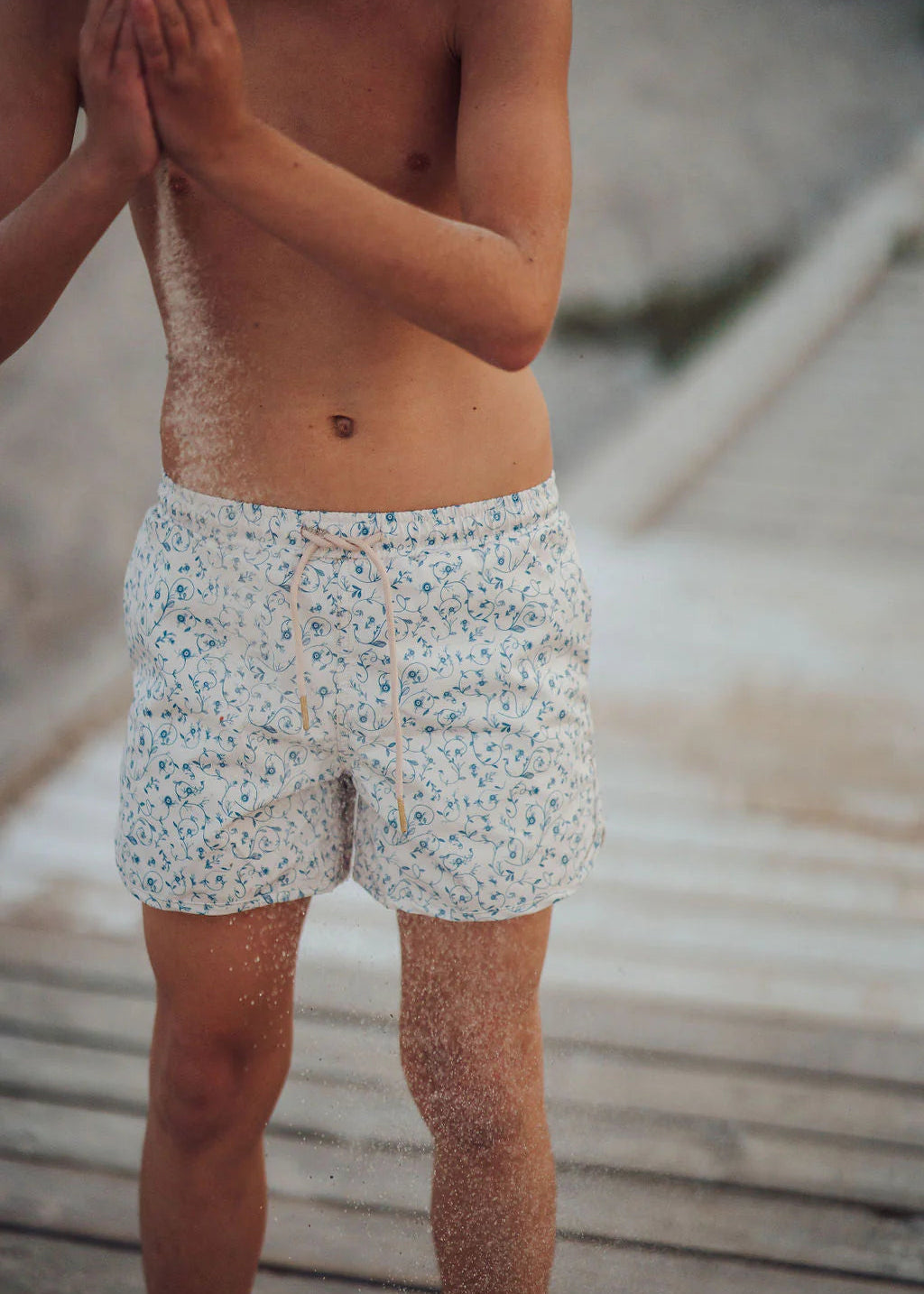 Person wearing patterned swim shorts standing on a wooden deck.