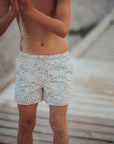 Person wearing patterned swim shorts standing on a wooden deck.