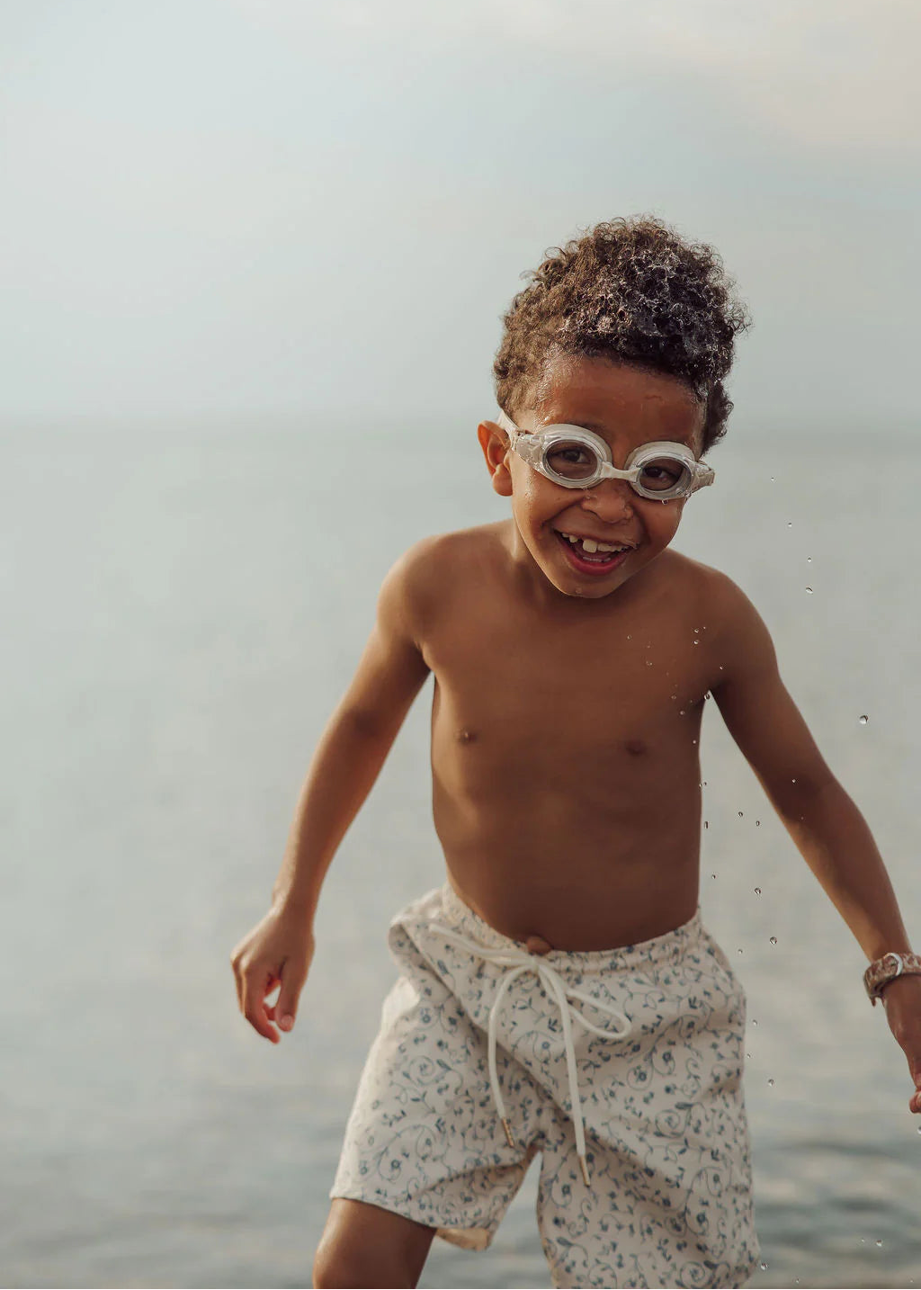 Child playing in water wearing swim goggles and a patterned towel around his waist.