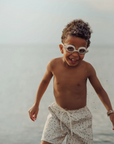 Child playing in water wearing swim goggles and a patterned towel around his waist.