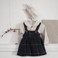 Children's outfit with black checkered dress, white shirt, and beige cardigan on a white surface.
