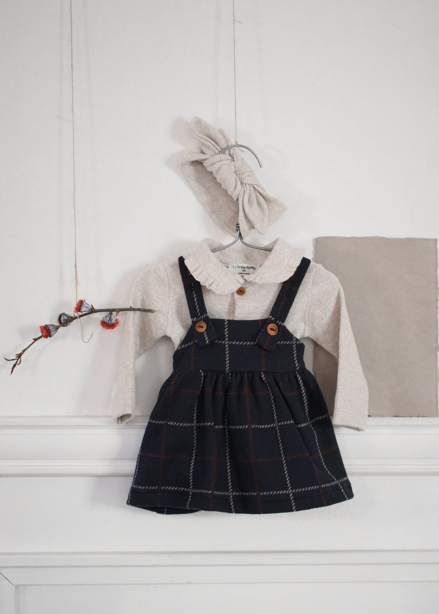 Children's outfit with black checkered dress, white shirt, and beige cardigan on a white surface.