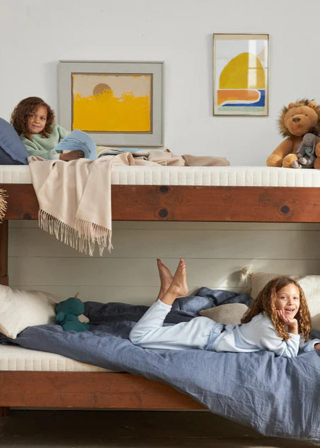 Children playing on a wooden bunk bed in a room with colorful artwork on the wall.