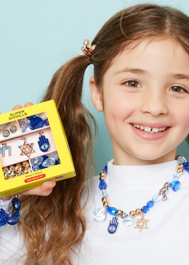 Young girl wearing a blue and gold necklace with a box of jewelry against a light blue background
