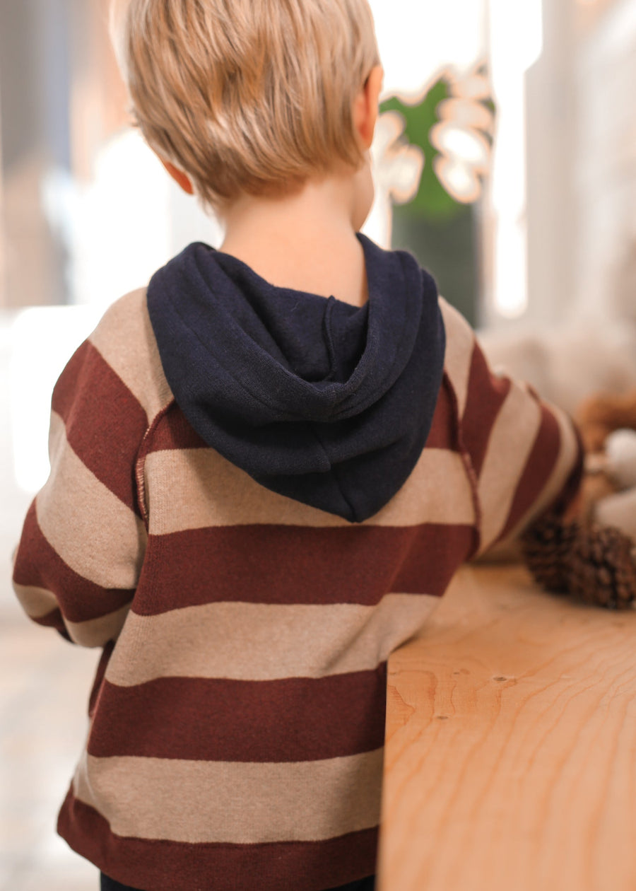Child wearing a striped sweater with a hood, standing indoors.