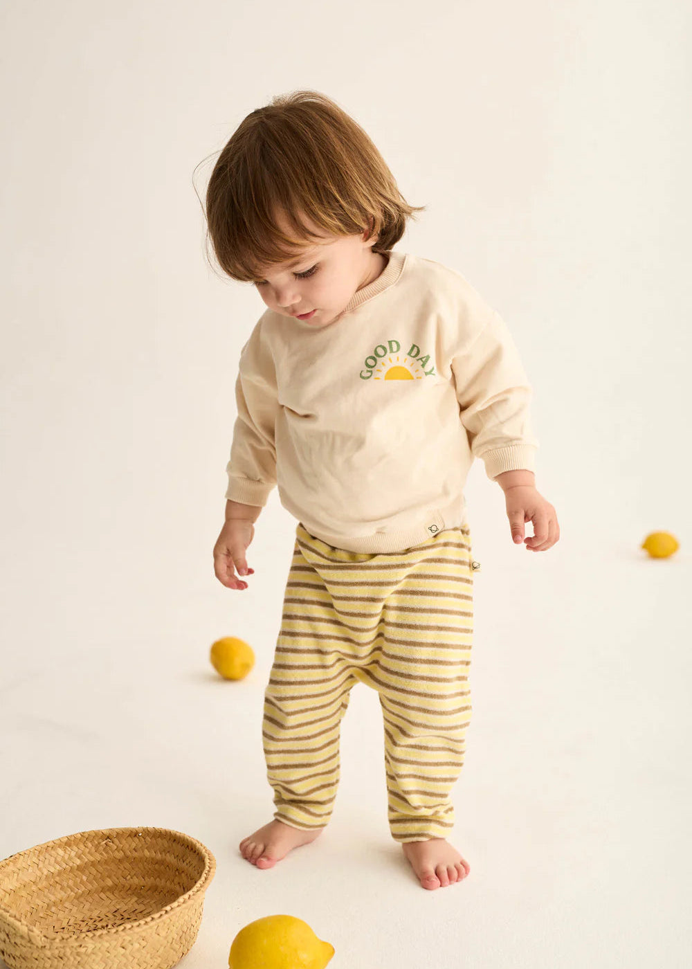 Child wearing a 'Good Day' shirt and yellow striped pants on a white background with lemons and a basket.