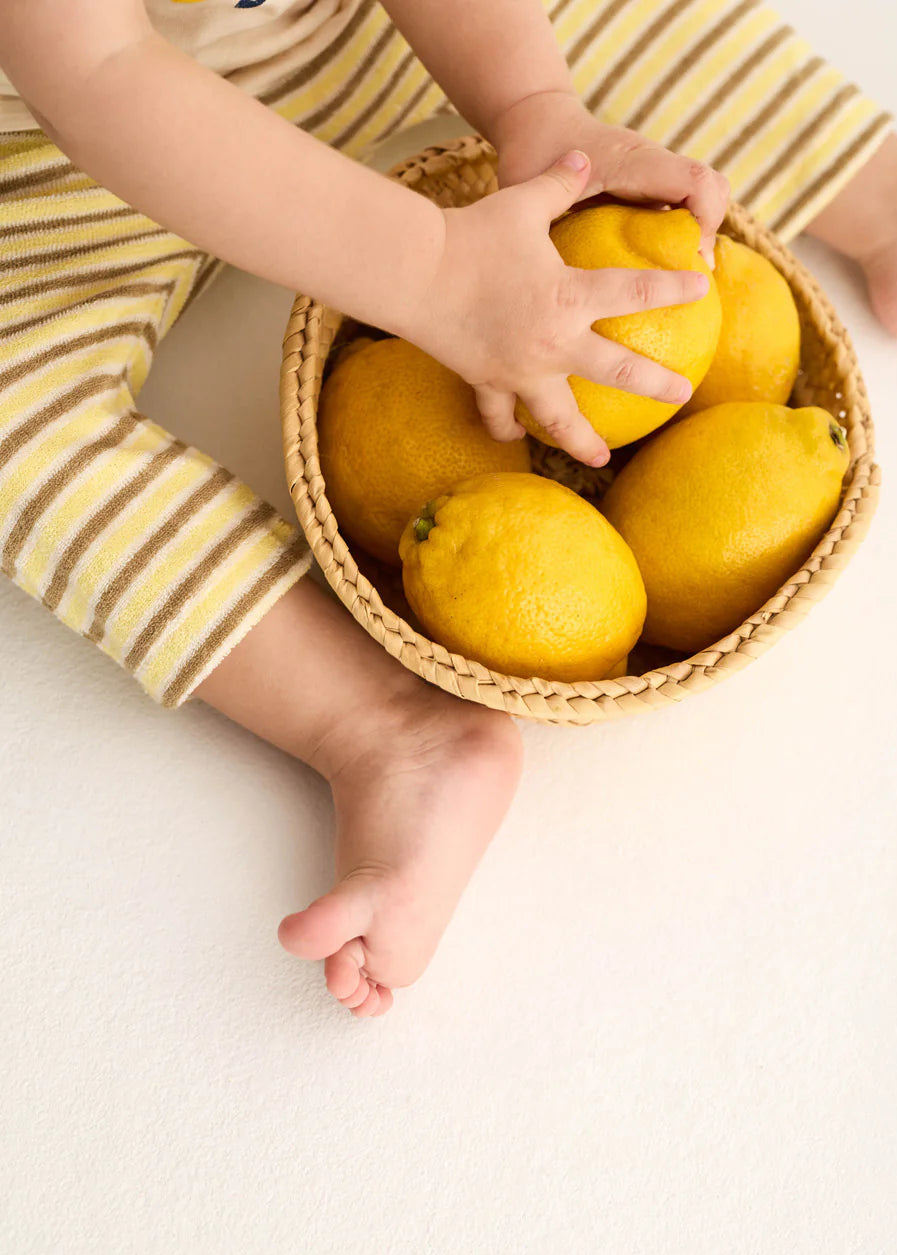 Child's hands reaching into a basket of lemons on a light surface