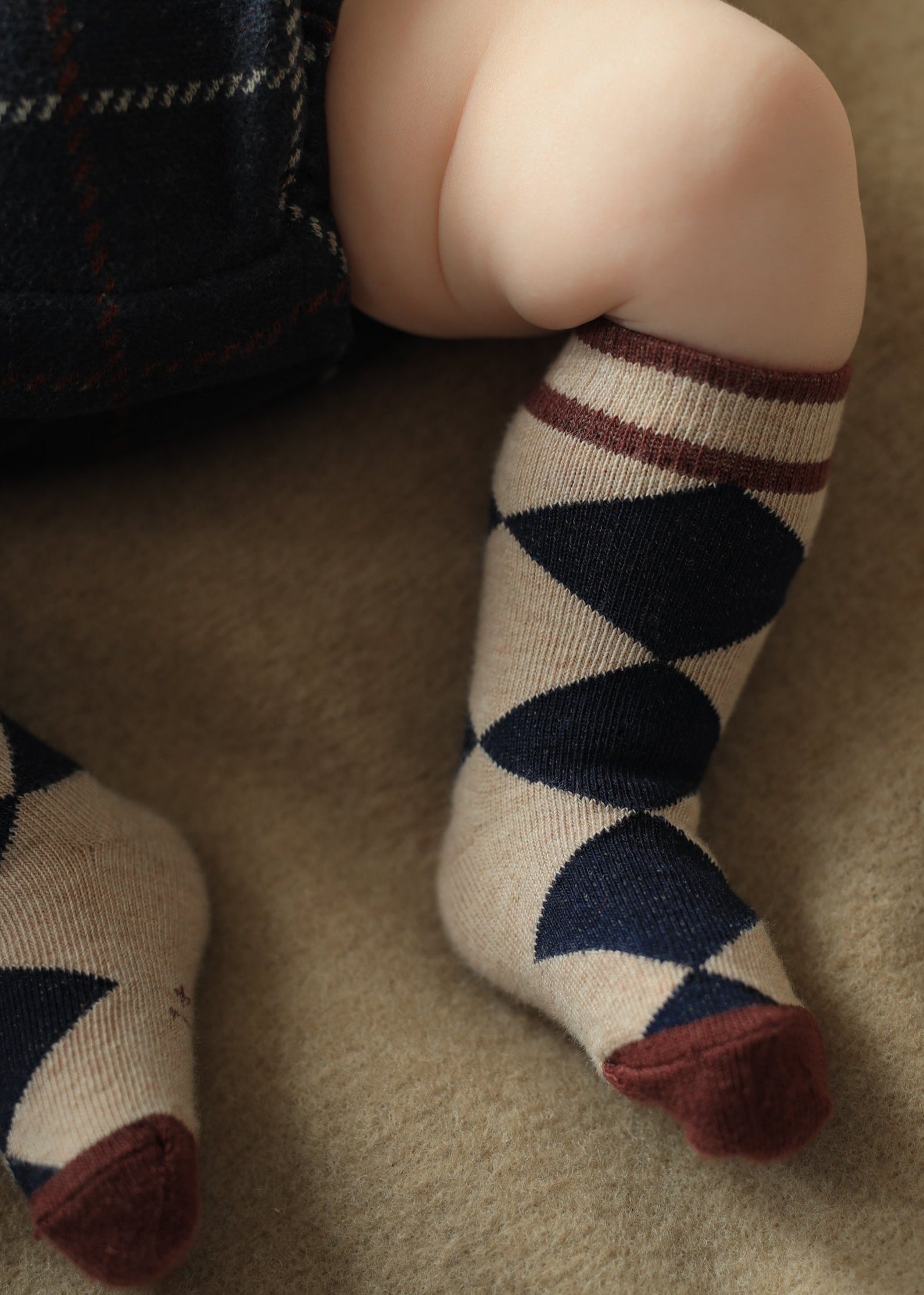 Children's legs wearing argyle patterned socks on a beige carpet
