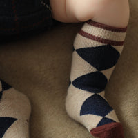Children's legs wearing argyle patterned socks on a beige carpet