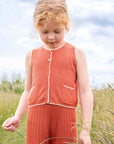 Young girl in a red outfit standing in a grassy field with a blue sky.