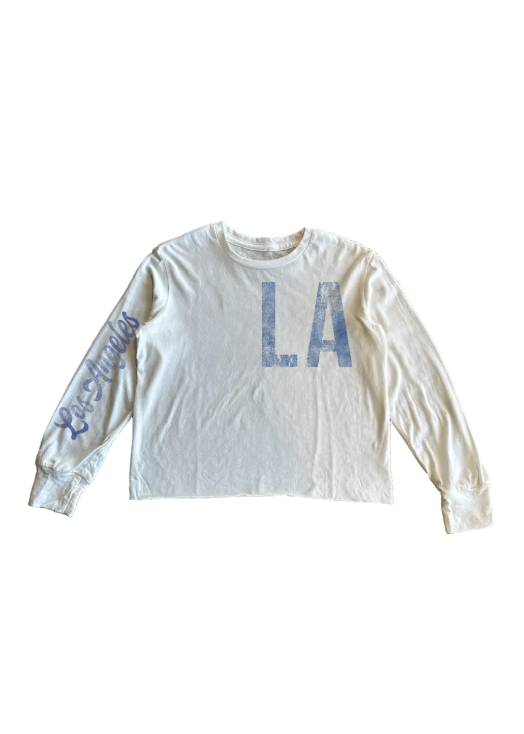 An off-white long-sleeve crop top featuring distressed blue 'LA' lettering on the chest and 'Los Angeles' script on the right sleeve, laid flat against a white background.