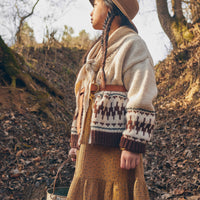 Person wearing a patterned sweater and hat in a forest setting