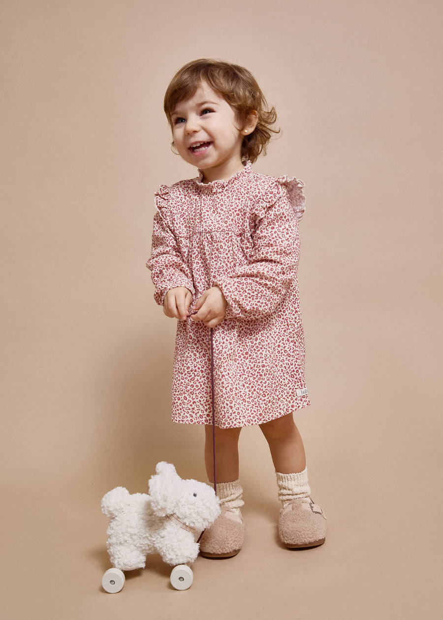 Child in a pink floral dress standing next to a white plush toy on a beige background