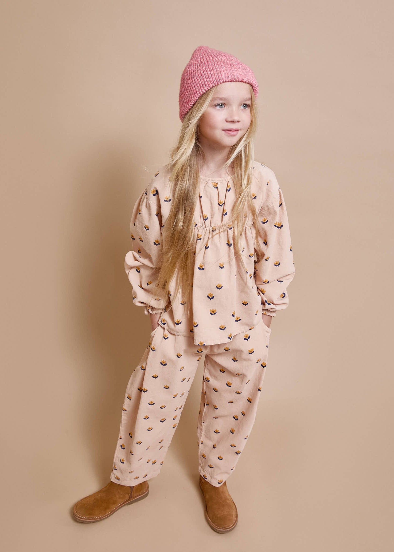 Young girl wearing a pink patterned outfit with a matching hat on a beige background