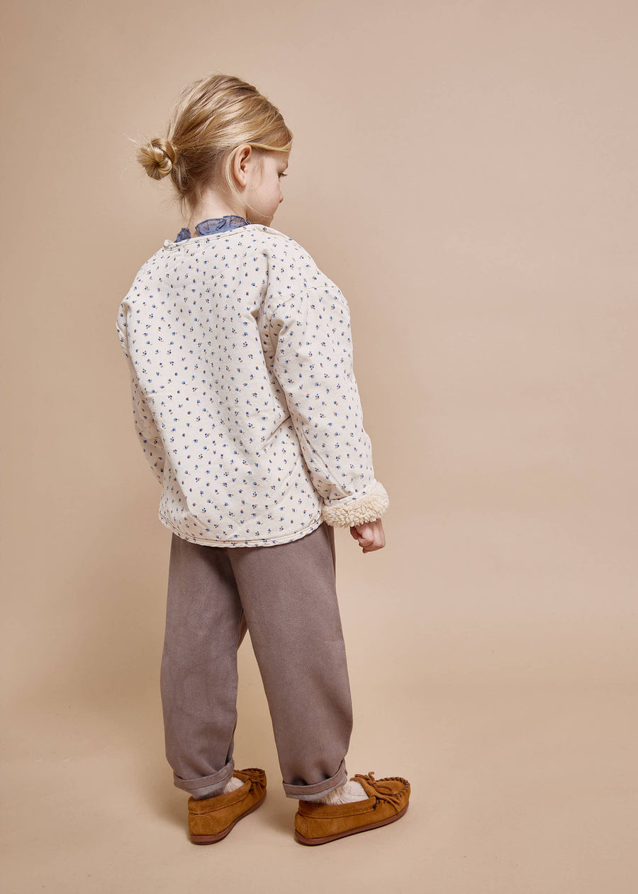 Child wearing a patterned shirt and brown pants on a beige background