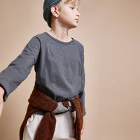 Child wearing a gray sweater, white pants, and a blue knitted hat against a beige background