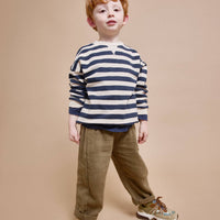 Young boy wearing a striped sweater and brown pants on a beige background