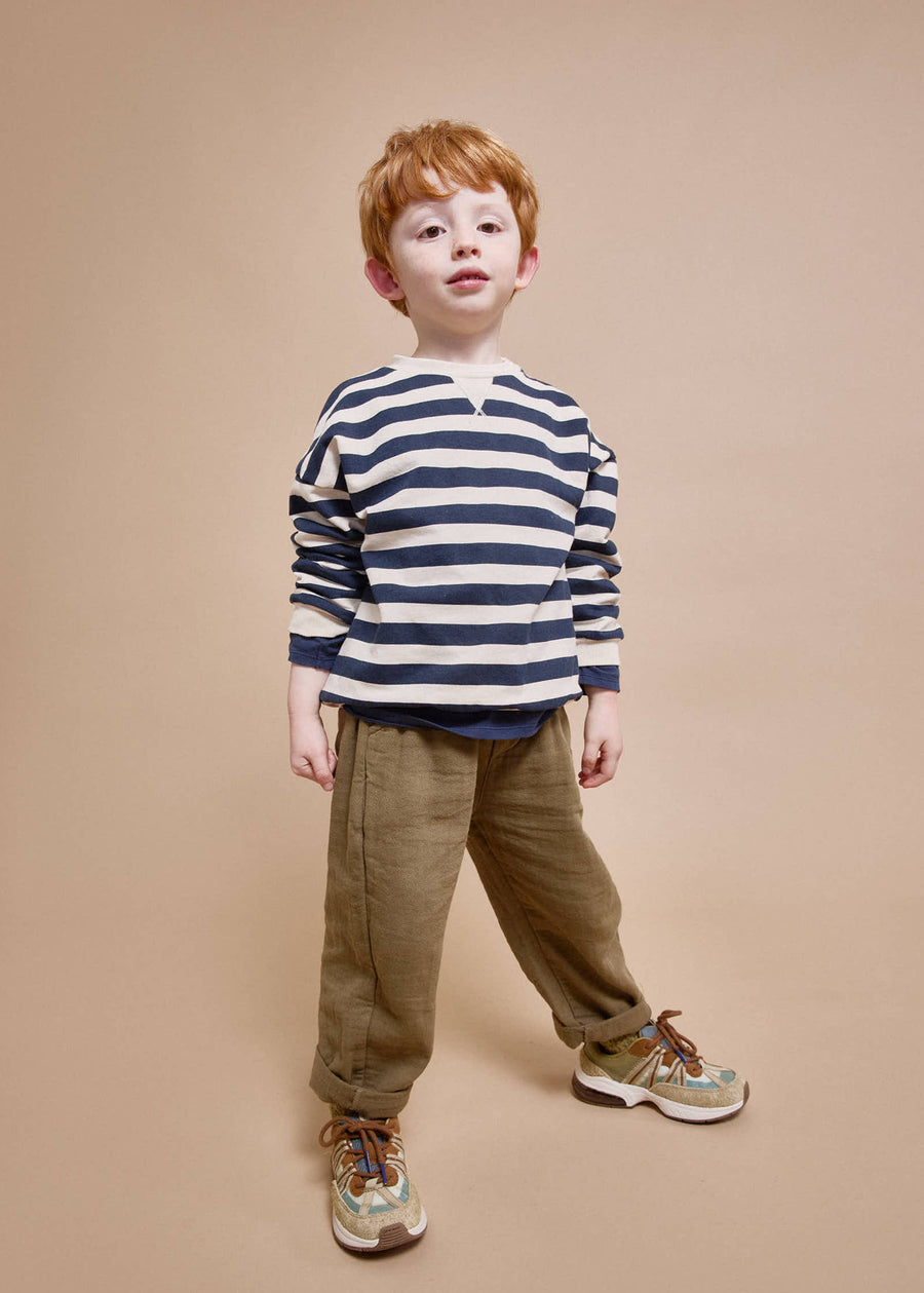 Young boy wearing a striped sweater and brown pants on a beige background