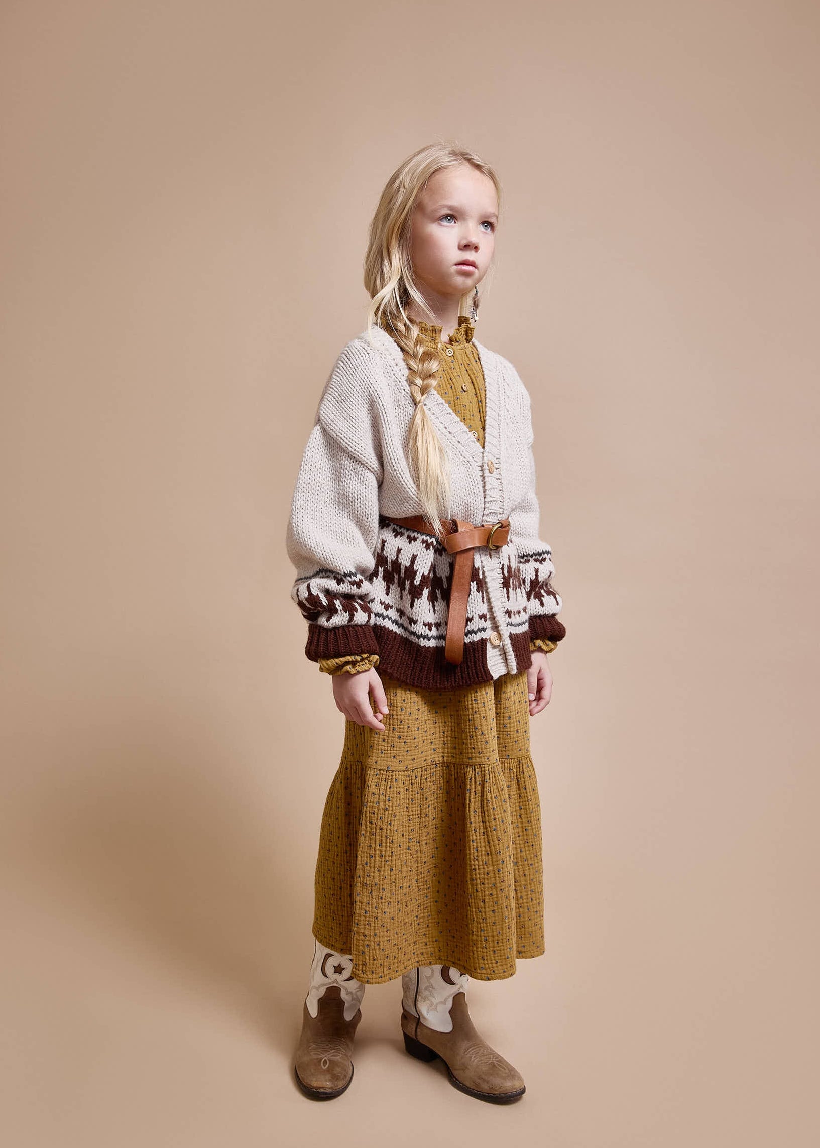 Young girl wearing a patterned sweater and mustard skirt against a beige background