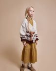 Young girl wearing a patterned sweater and mustard skirt against a beige background