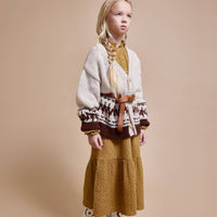 Young girl wearing a patterned sweater and mustard skirt against a beige background