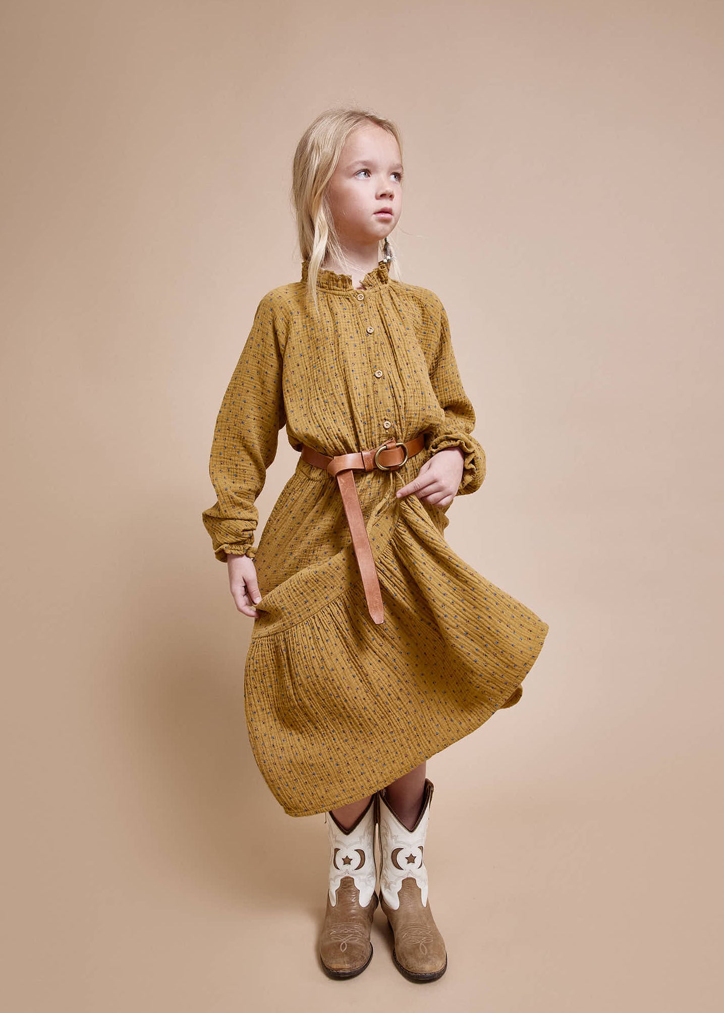 Girl wearing a mustard yellow dress with a belt on a beige background