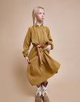 Girl wearing a mustard yellow dress with a belt on a beige background