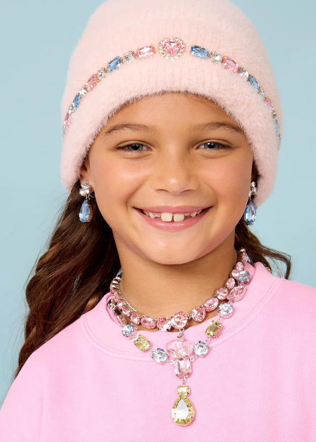 Young girl wearing a pink beanie and jewelry set against a light blue background