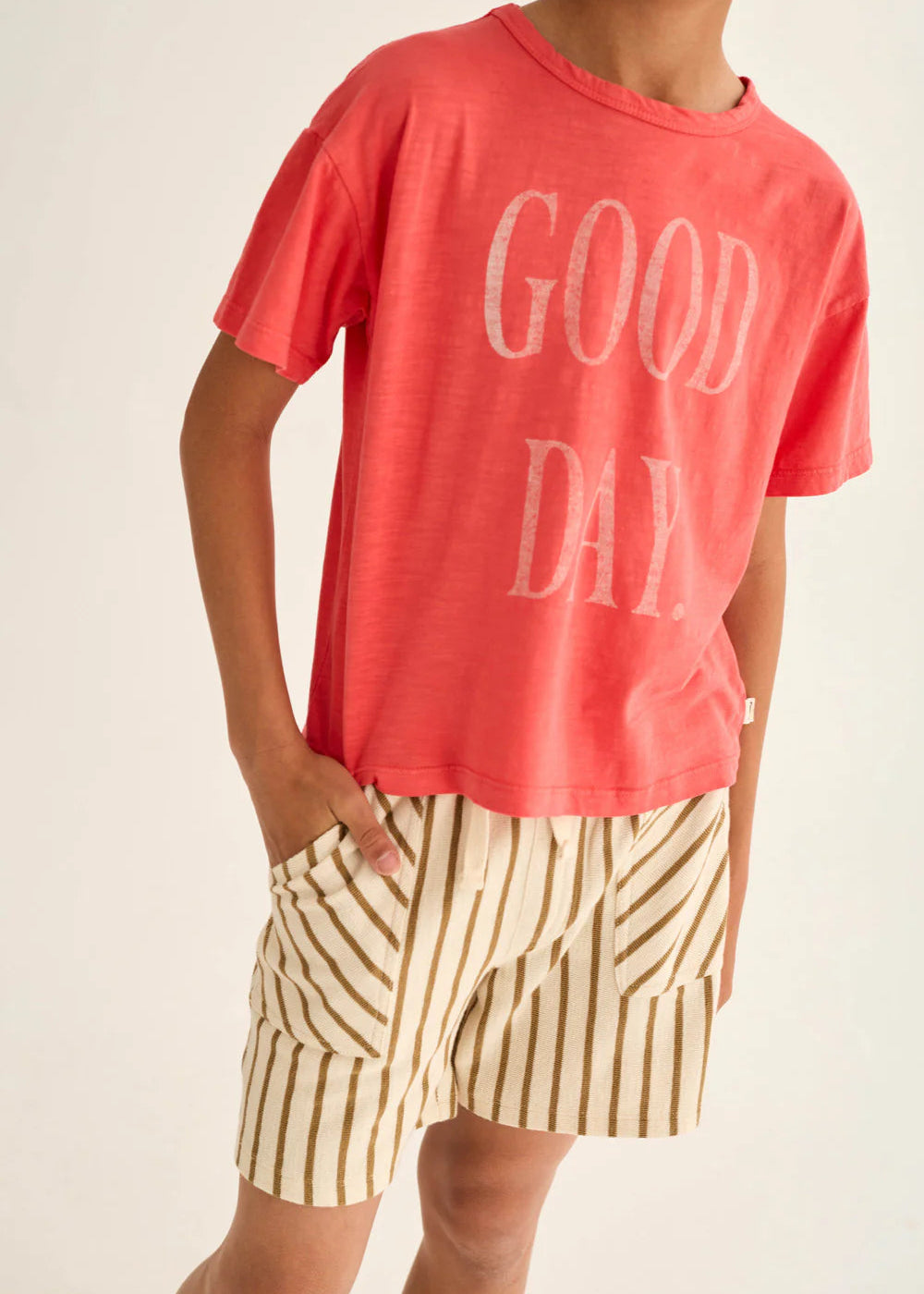 Person wearing a red 'GOOD DAY' t-shirt and striped shorts on a plain background
