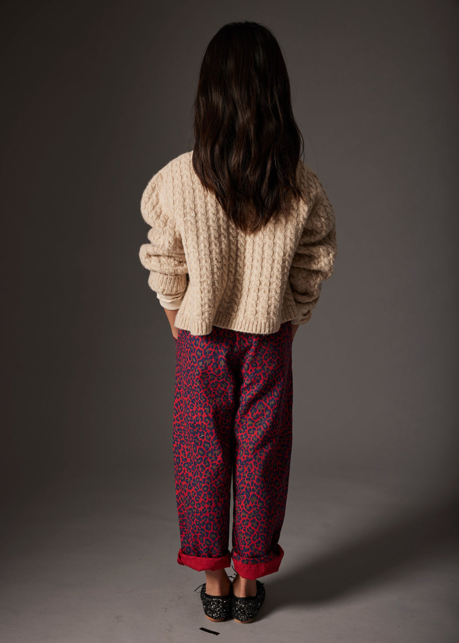 Person wearing a beige sweater and red patterned pants standing against a gray background