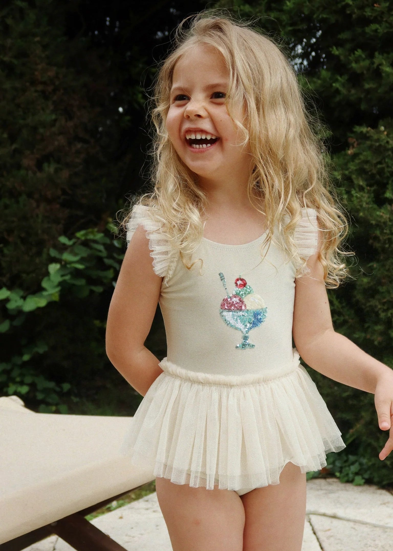 Young girl in a white dress with ruffled sleeves and a skirt, standing outdoors.