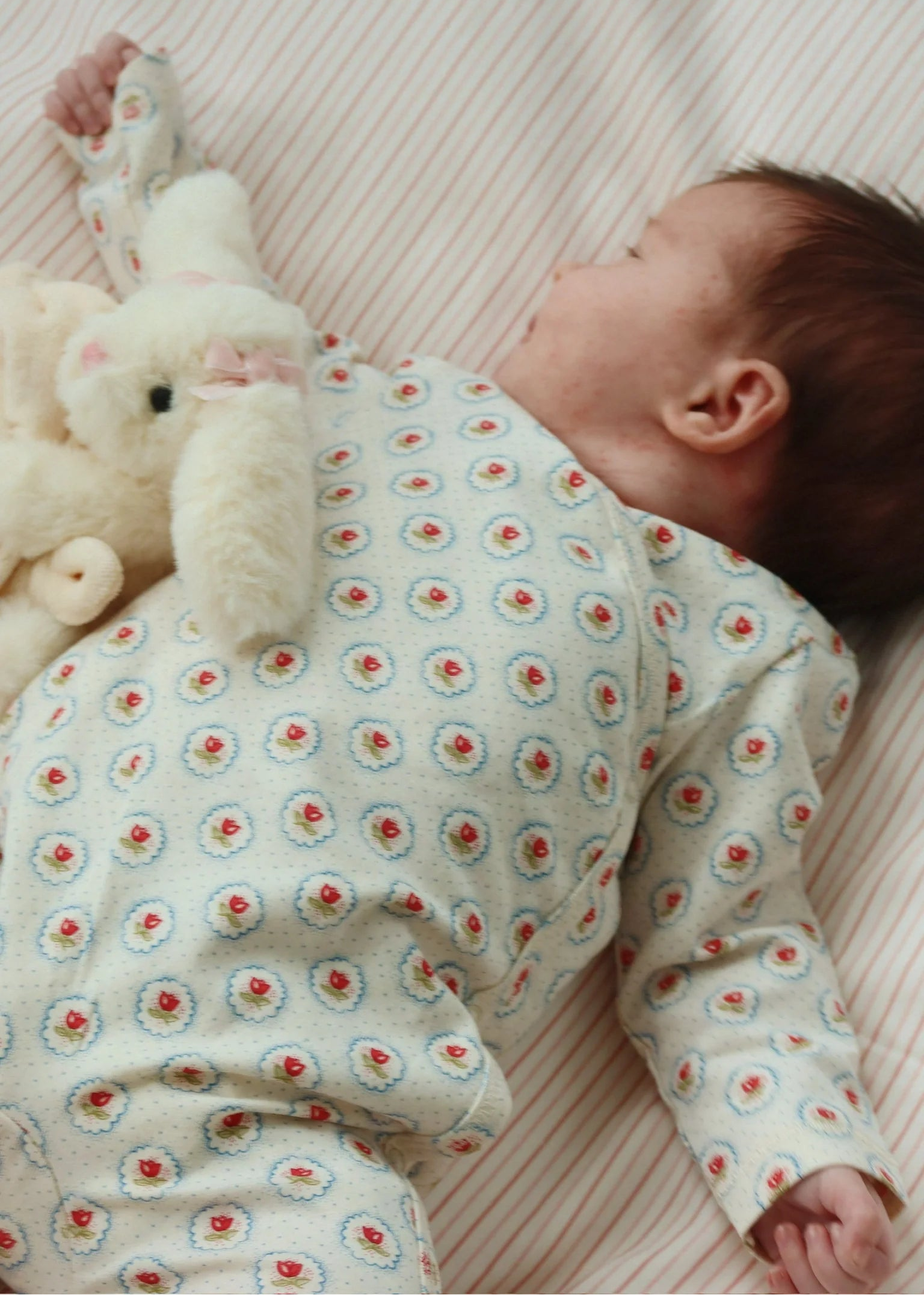 Baby lying on a blanket with a floral-patterned outfit and a plush toy.