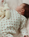Baby lying on a blanket with a floral-patterned outfit and a plush toy.