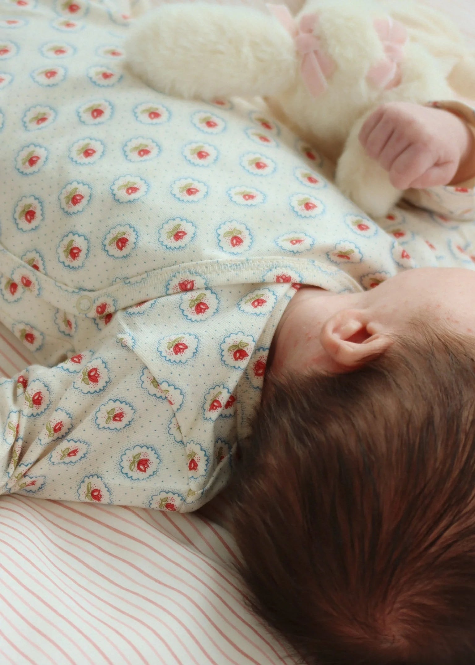Baby wearing a floral onesie lying on a striped surface