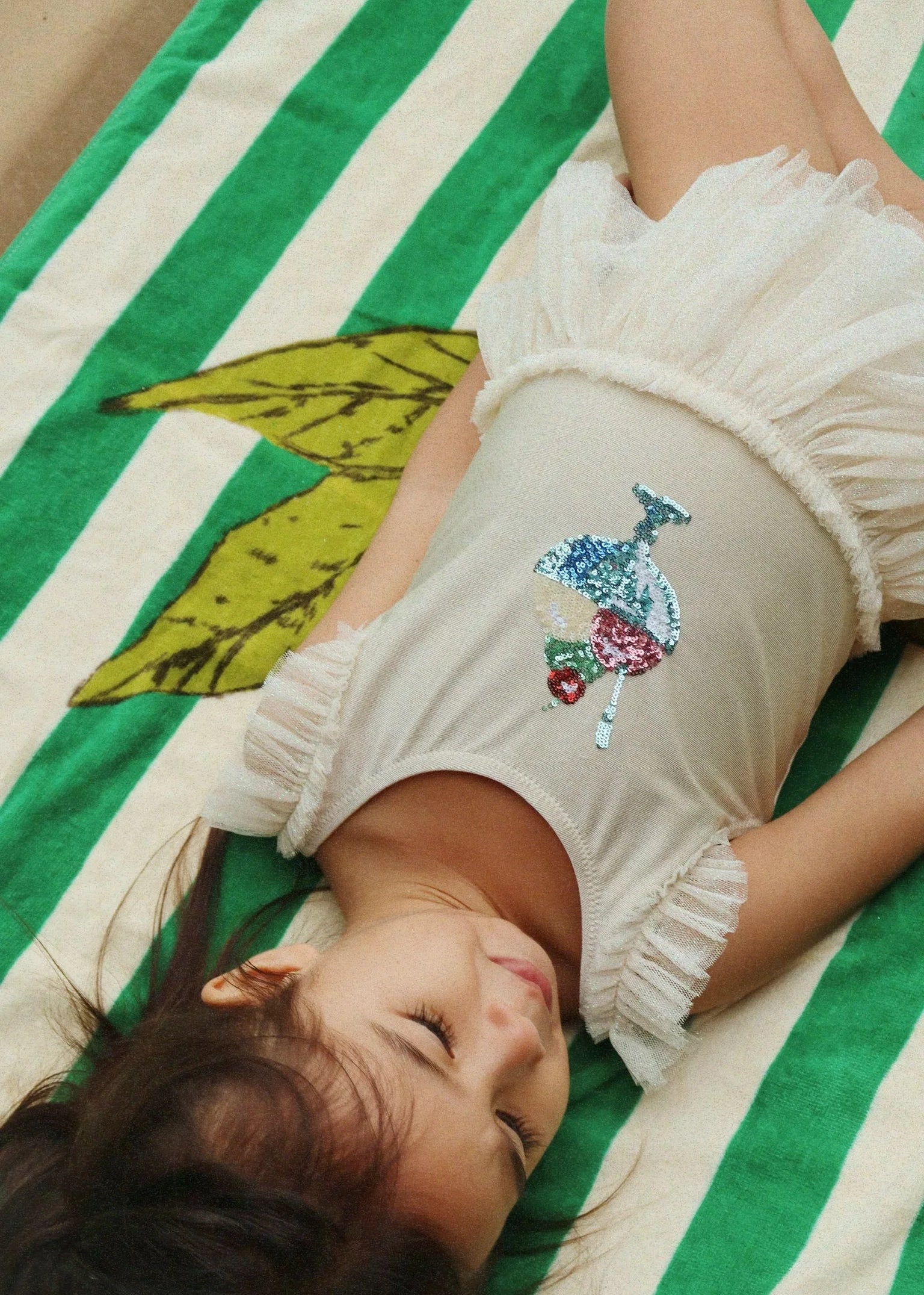 Child lying on a green and white striped blanket with a floral design.