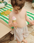 Child holding an ice cream cone on a sandy surface with a striped towel and pool float in the background.