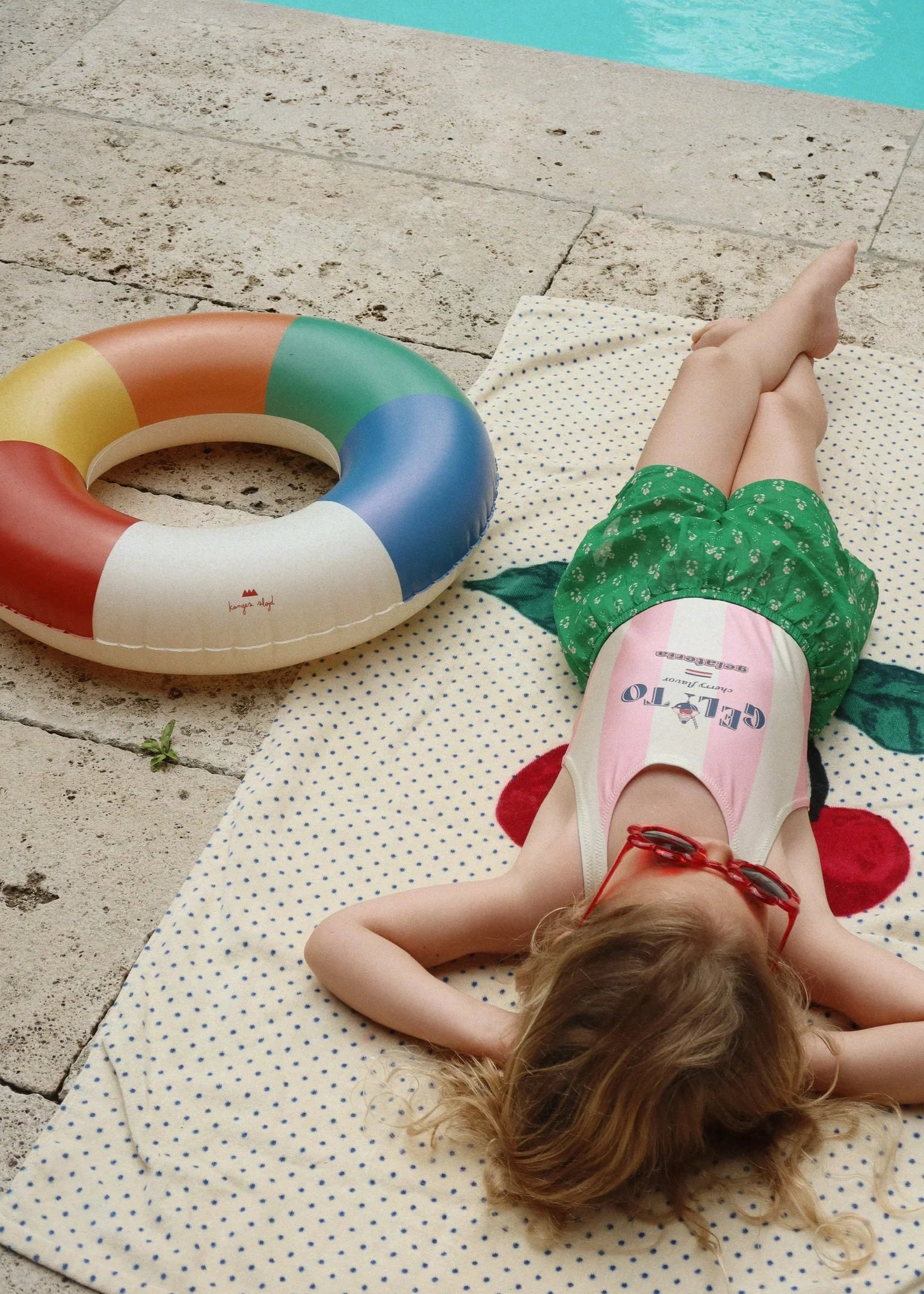 Person lying on a towel next to a colorful inflatable ring by a pool.