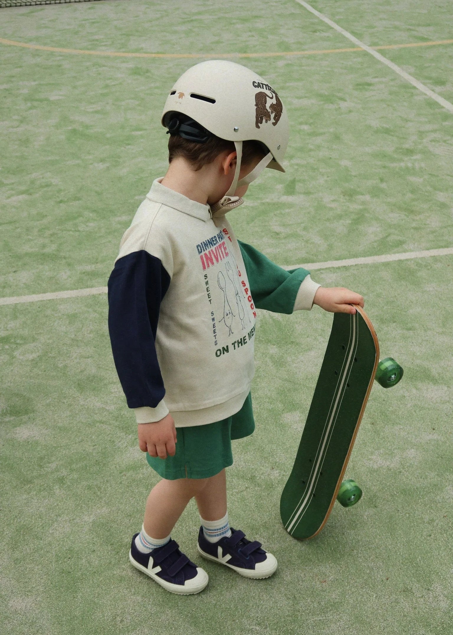 Child wearing a helmet and holding a skateboard on a tennis court