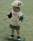 Child wearing a helmet and a sweatshirt with text, standing on a skateboard on a green surface.