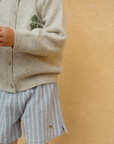 Child wearing a beige cardigan and striped shorts against a yellow background