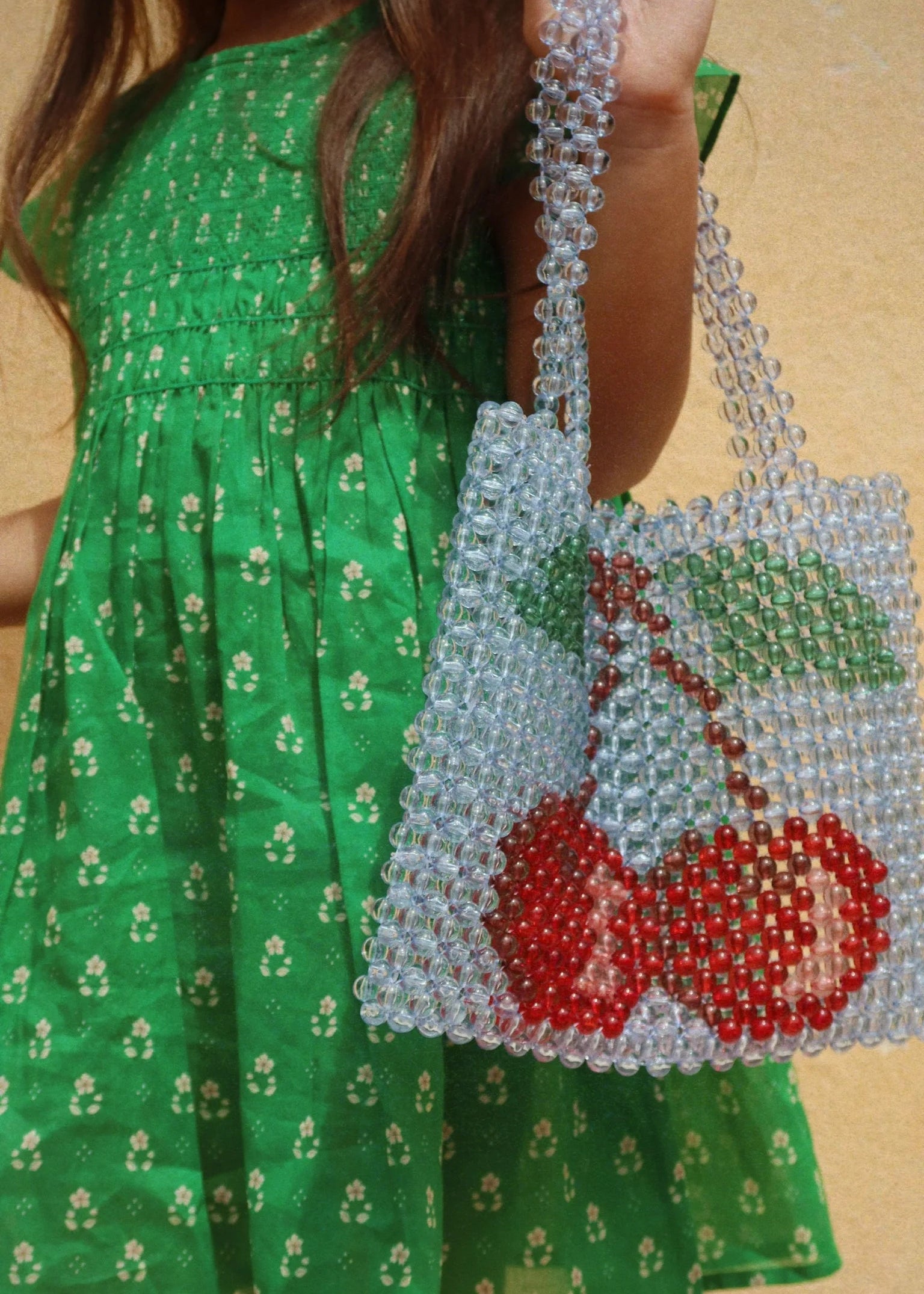 Person wearing a green dress holding a beaded bag with cherry design.