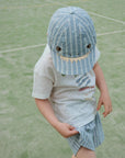 Child wearing a blue shark-themed cap and outfit on a green outdoor surface
