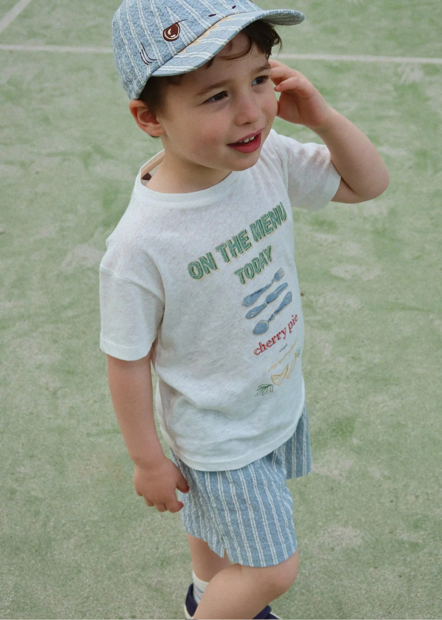 Child wearing a cap and t-shirt with text on a grassy background