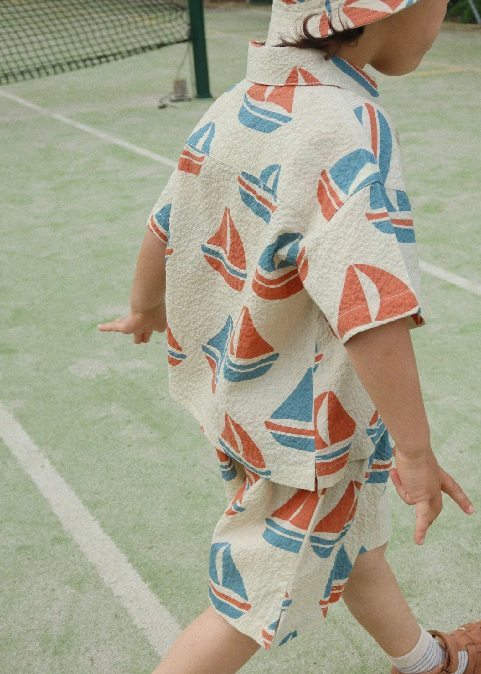 Child wearing a towel with sailboat pattern on a tennis court