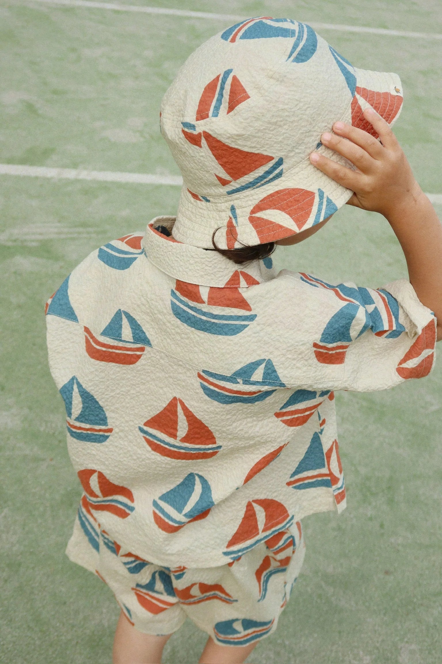 Child wearing a boat-patterned raincoat on a green surface
