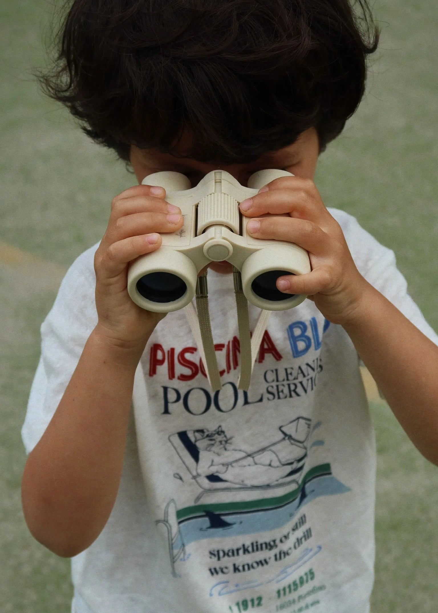 Child holding binoculars with a vintage pool service t-shirt in the background