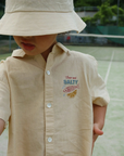 Child wearing a beige hat and shirt with 'Salty' branding on a tennis court.