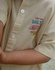 Beige shirt with 'Four and Salt' logo on a blurred background