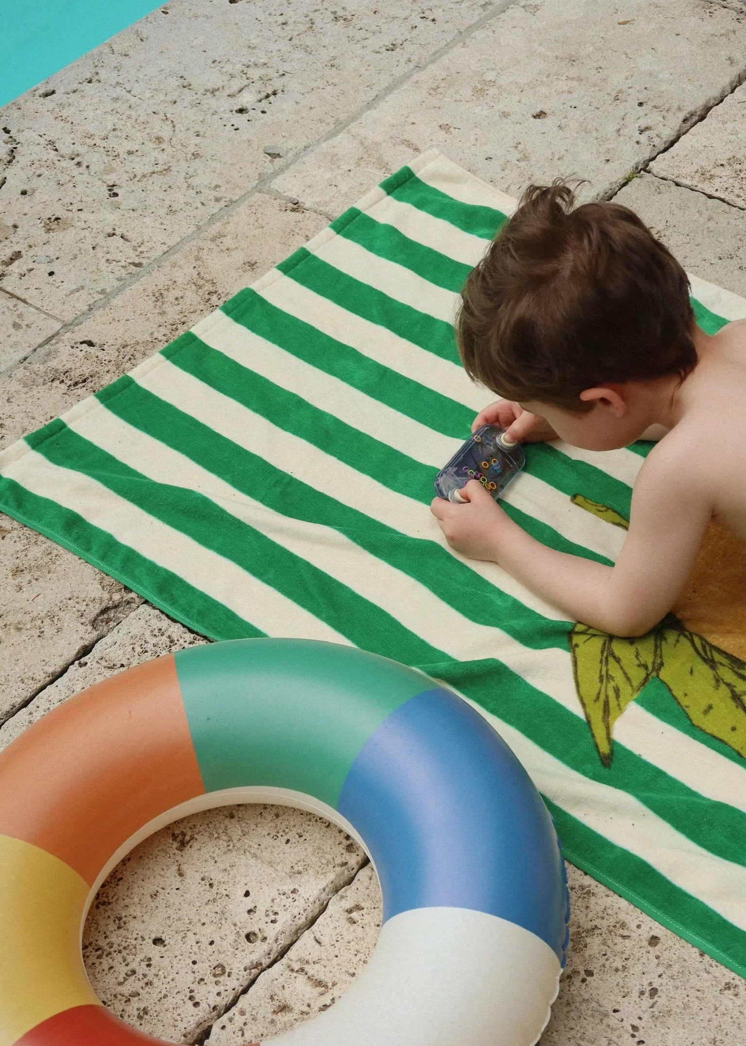 Child playing on a green and white striped towel with a colorful inflatable ring nearby.