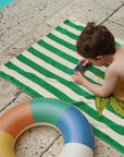 Child playing on a green and white striped towel with a colorful inflatable ring nearby.